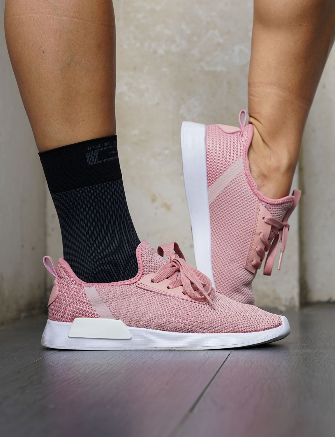 Pair of feet with one wearing black Neo G Airflow Ankle Support under pink shoes