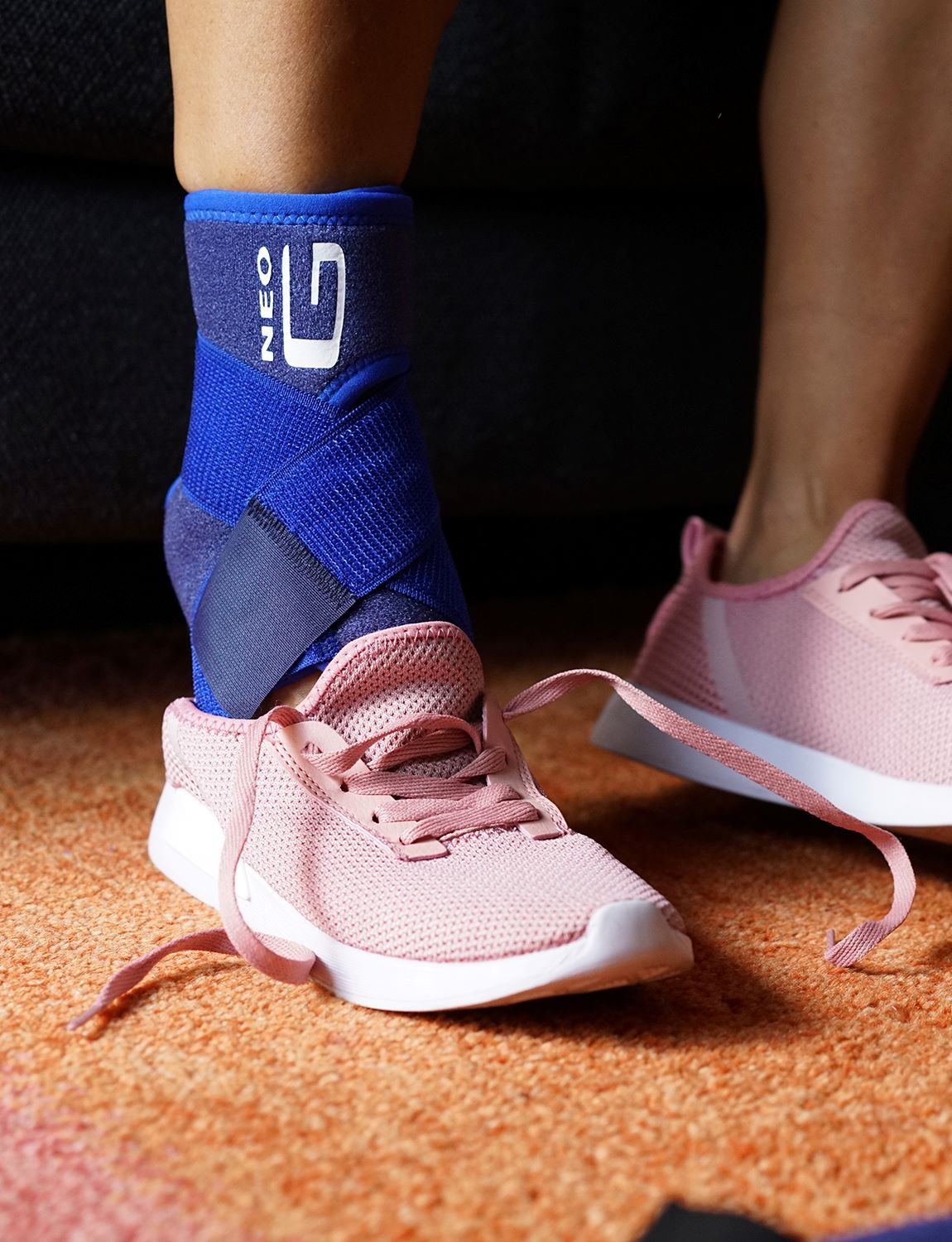 Woman wearing Neo G Ankle Support with Figure of 8 Strap putting on pink sneakers