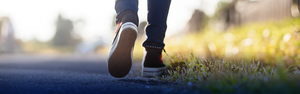 An image cropped to a mans feet wearing canvas sneakers walking on a path beside some grass