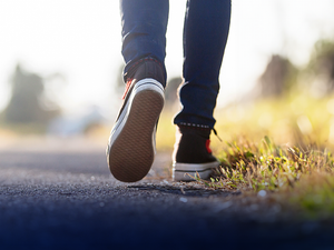 An image cropped to a mans feet wearing canvas sneakers walking on a path beside some grass